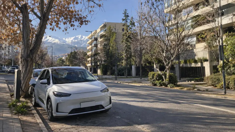 Auto eléctrico estacionado en una calle arbolada de Providencia con la cordillera nevada al fondo
