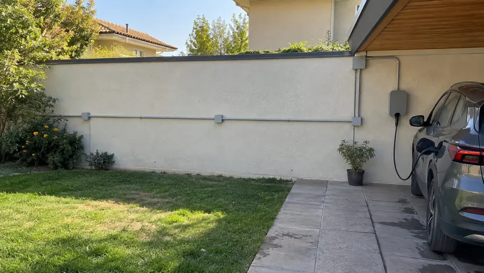 Canalización eléctrica gris por el muro del patio hasta un cargador bajo el alero